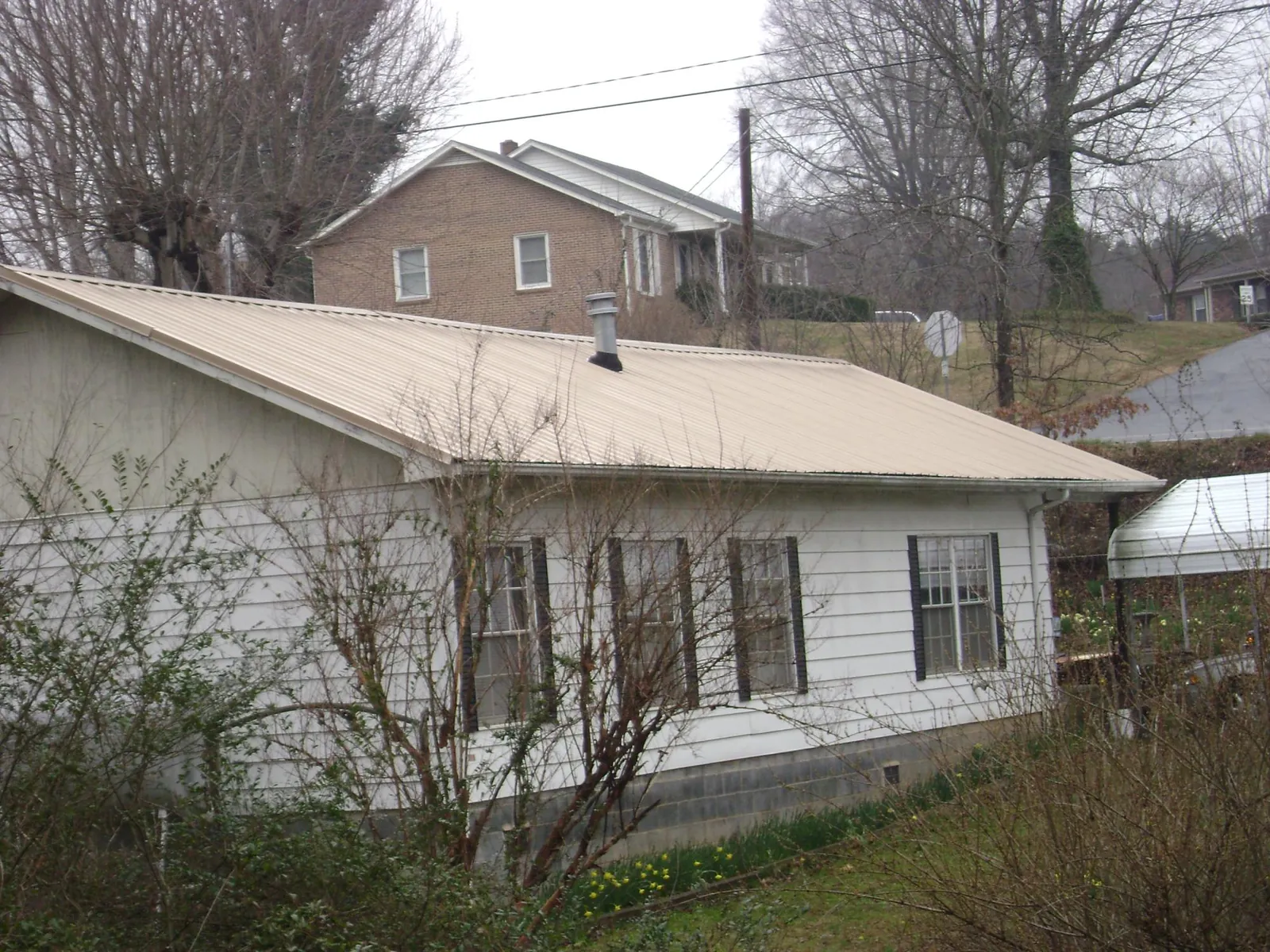 Tan metal roof on a white sided house set into a hillside — Commercial Roofing by Roofing Brothers in Church Hill